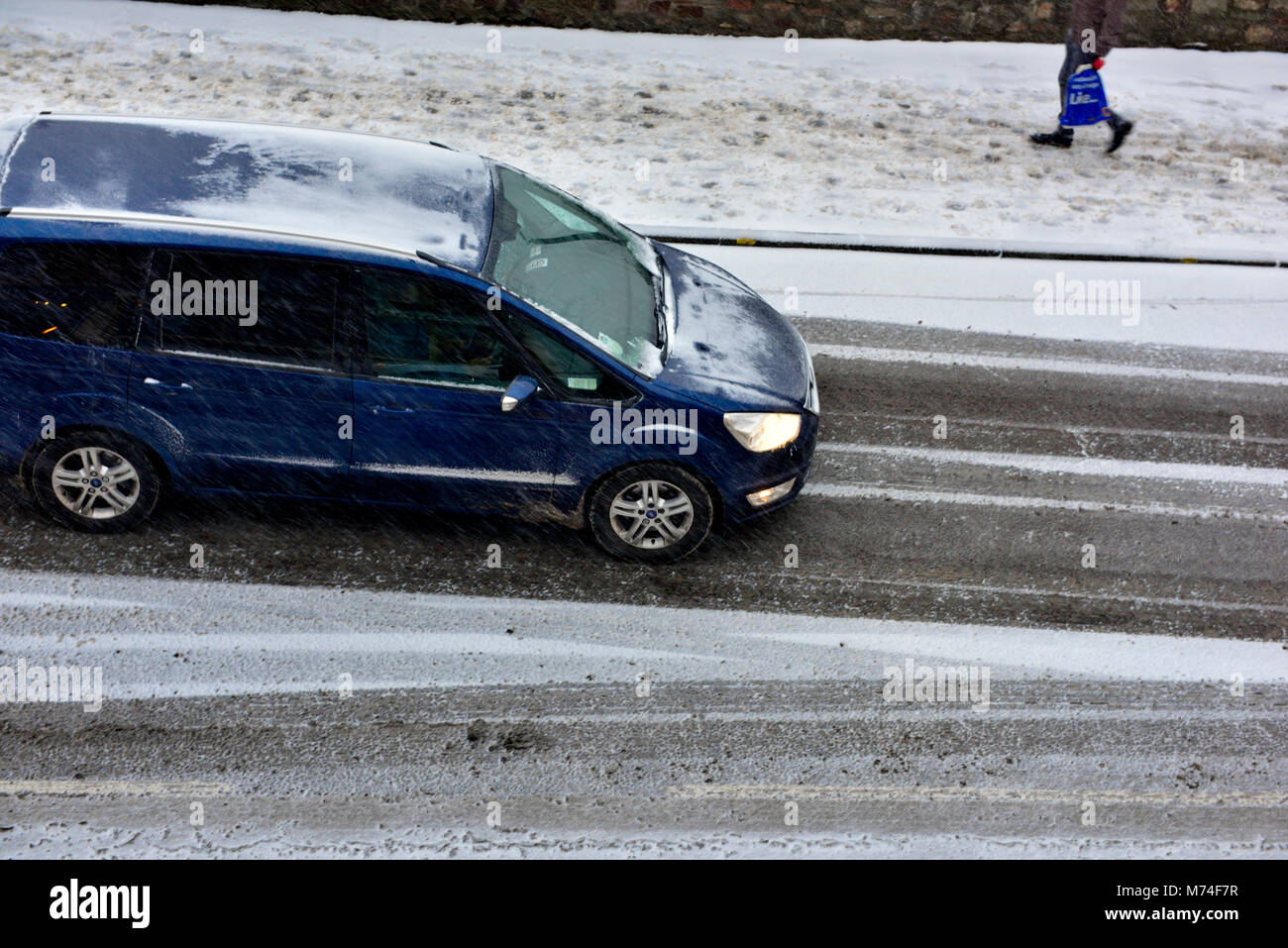 Auto e pedoni di luce neve con tracce di auto su strada Foto Stock
