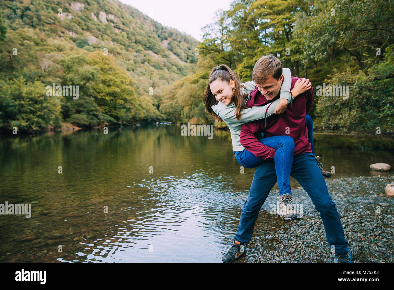 Ragazzo adolescente ha la sua sorella in una piggy back attesa e finge di buttarla in un lago mentre sono fuori escursionismo. Foto Stock