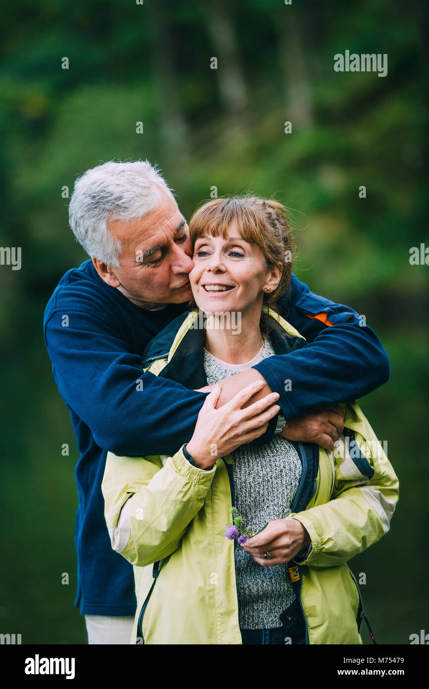 Coppia senior sono in posa per la telecamera durante le escursioni. L'uomo sta baciando la moglie con le sue braccia avvolto attorno a lei. Foto Stock