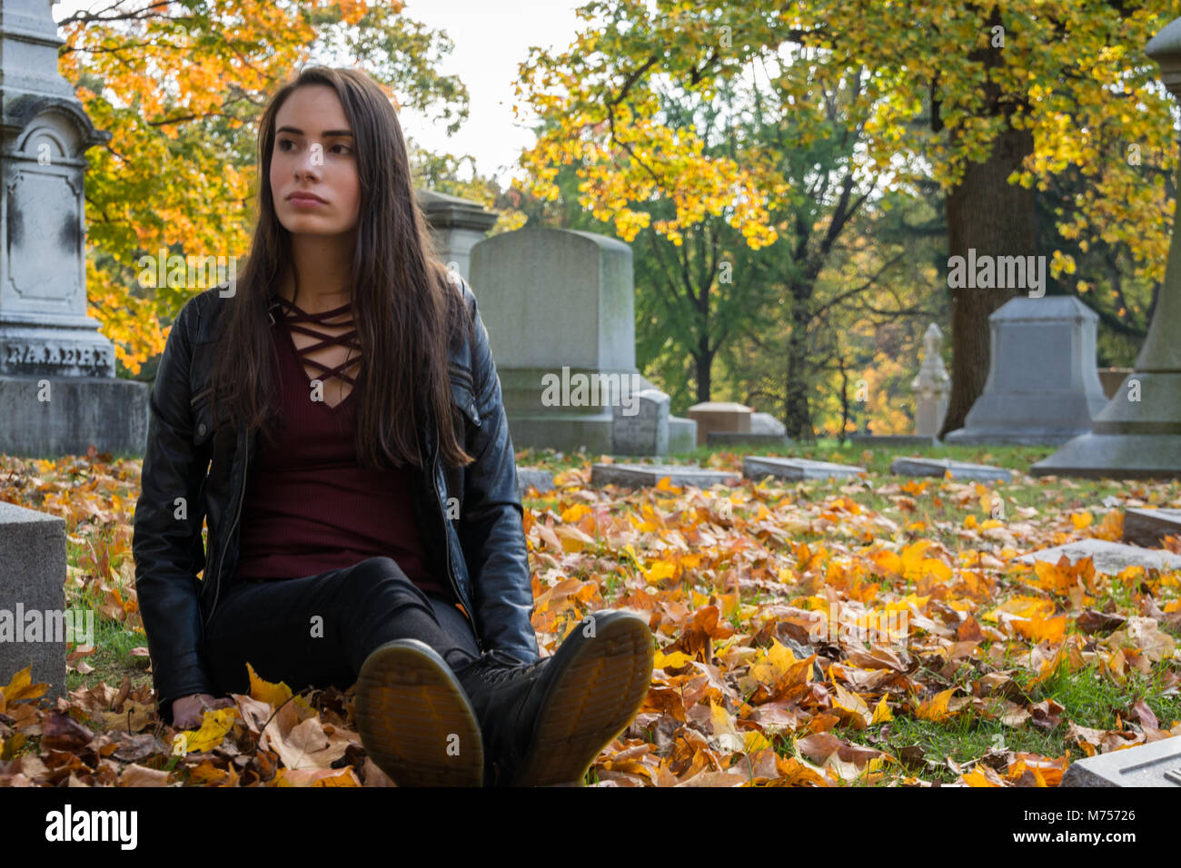 Una giovane ragazza serena riflessione, il lutto, ricordando il significato della vita e della morte, la stagione autunnale, circondato da foglie, tristezza. Foto Stock