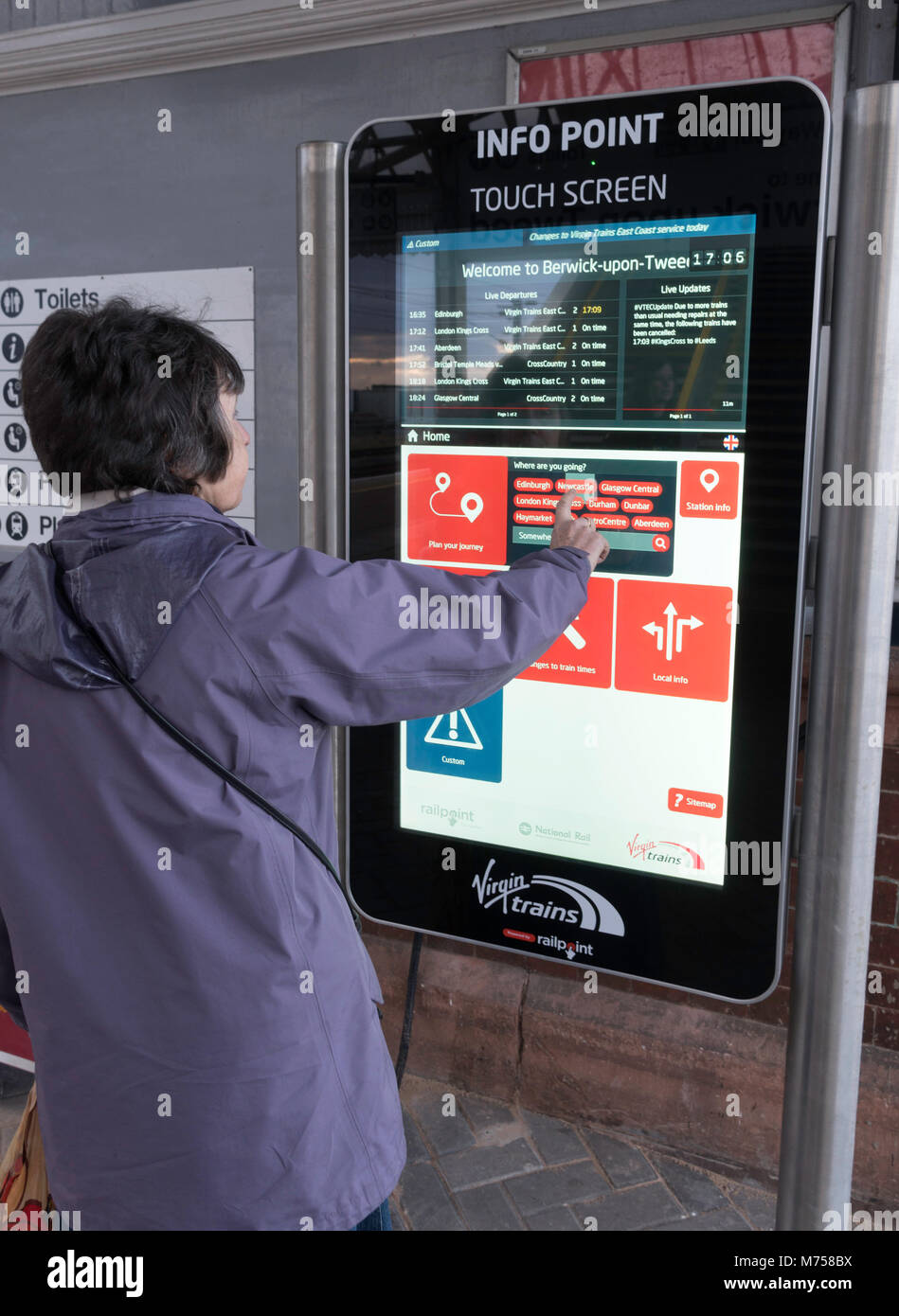 Donna che utilizza punto Info display di schermo a sfioramento sul Berwick upon Tweed stazione ferroviaria, Northumberland, England, Regno Unito Foto Stock