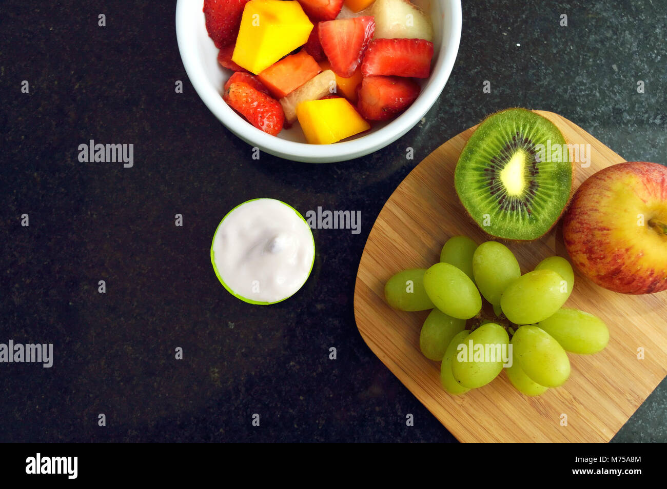 Ciotola con insalata di frutta e alcuni yogurt su un bancone di granito visto da direttamente sopra Foto Stock