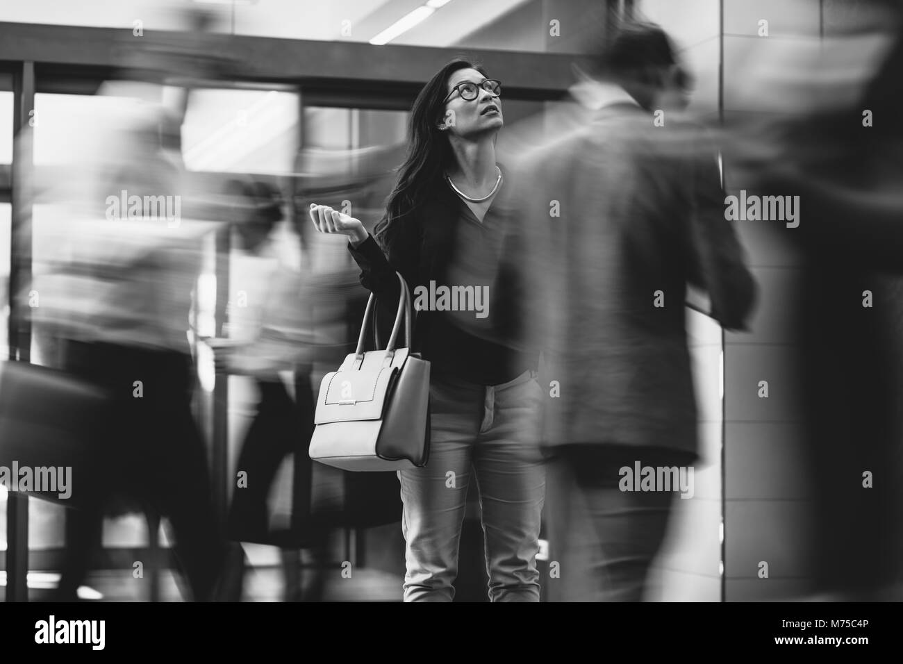 Imprenditrice asiatici in attesa di qualcuno con gente correre nella lobby. Motion Blur effetto. In bianco e nero girato. Foto Stock