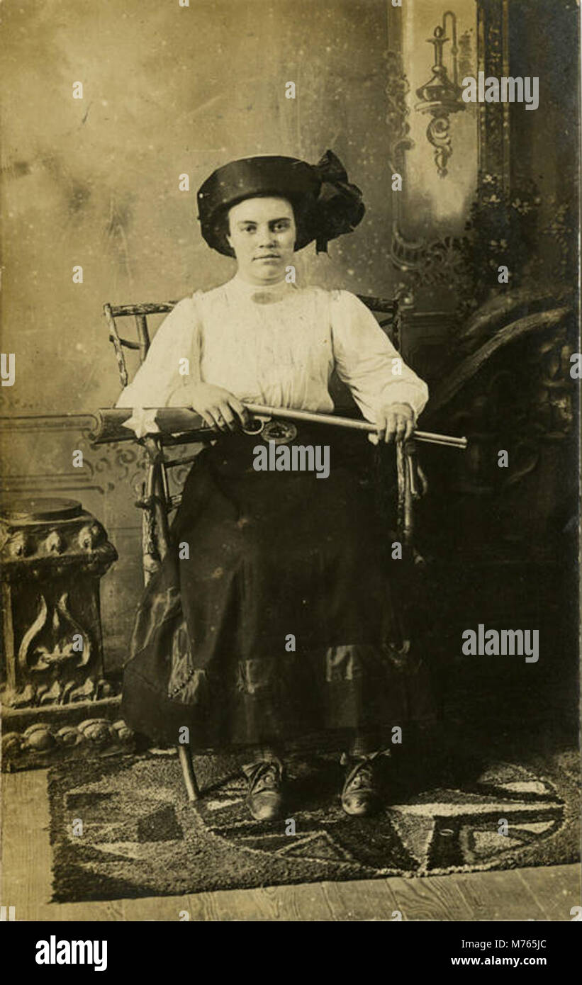 Un'immagine storica di una donna armata del 1911, che detiene quello che sembra essere un fucile ad aria compressa, forse una rappresentazione di donne in contesti all'inizio del XX secolo come la caccia o le attività all'aperto. Foto Stock