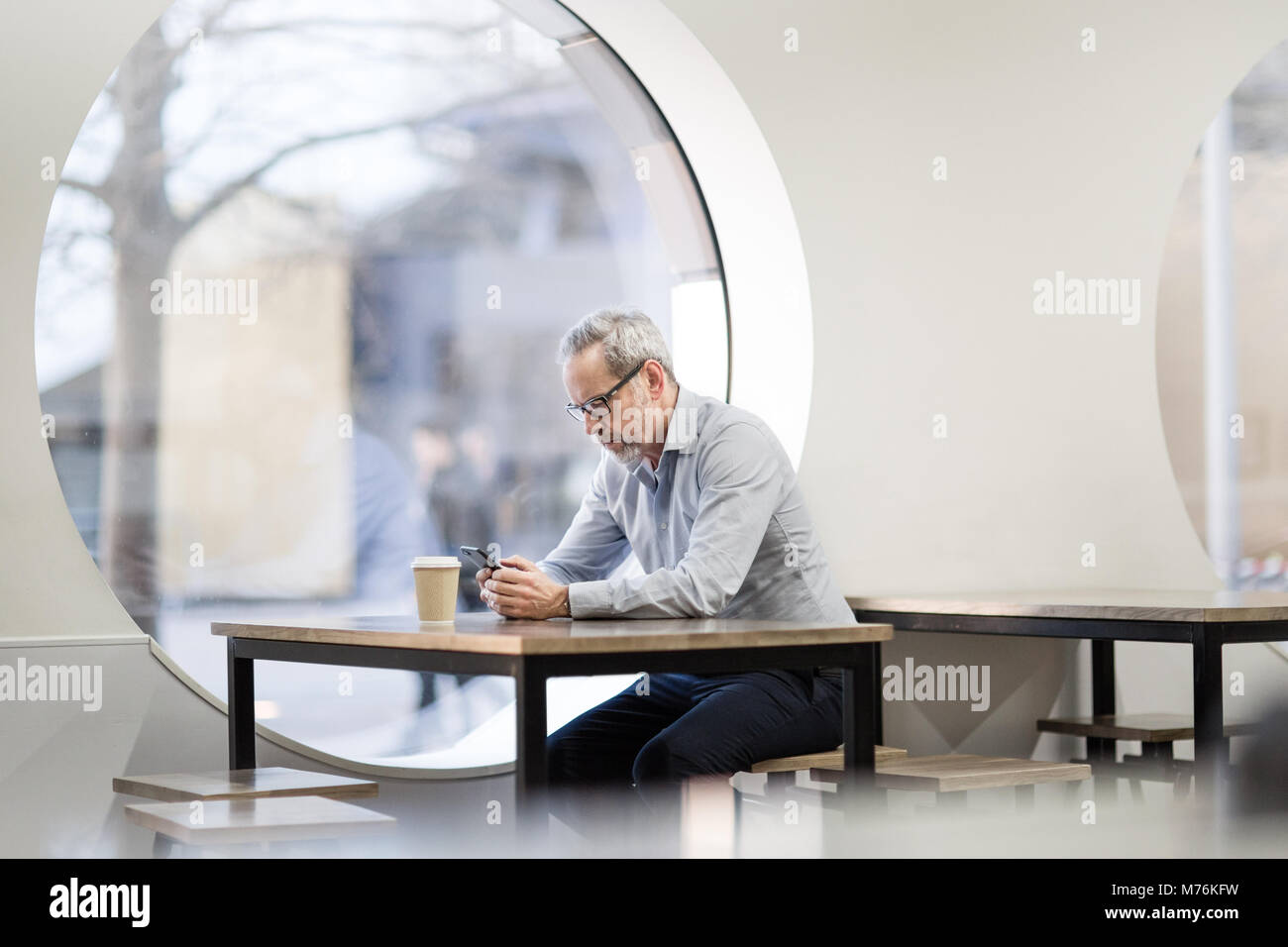 Imprenditore in attesa in cafe smartphone di controllo Foto Stock
