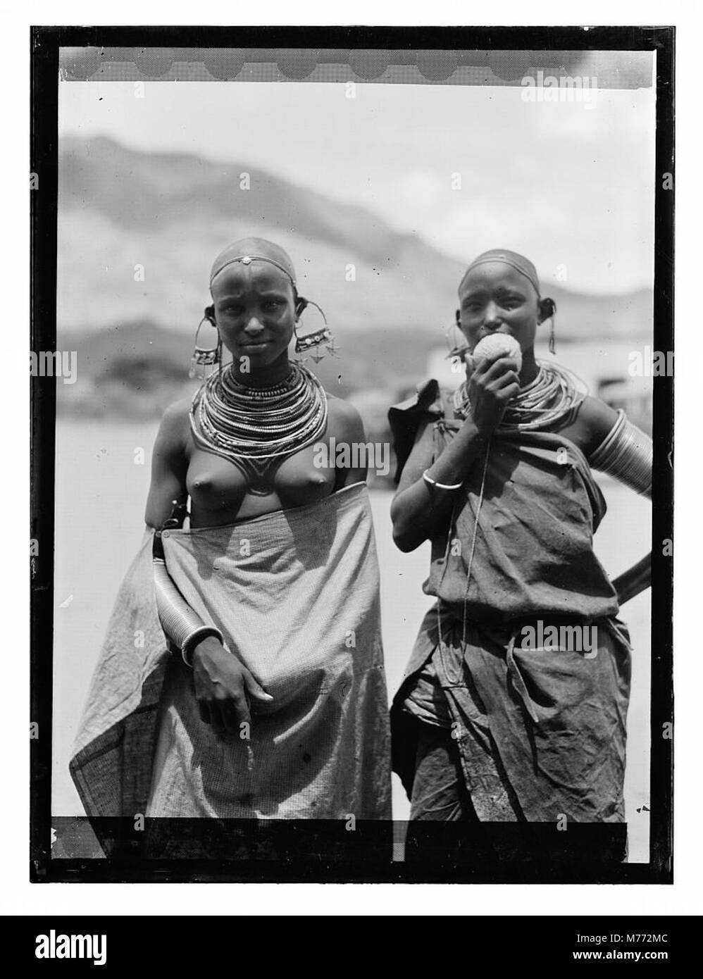 Fotografia di ragazze Longido in Tanganica (ora parte della Tanzania), che indossano grandi ornamenti per orecchie. L'immagine mette in risalto l'abbigliamento e le pratiche culturali tradizionali della regione durante i primi anni del XX secolo. Foto Stock
