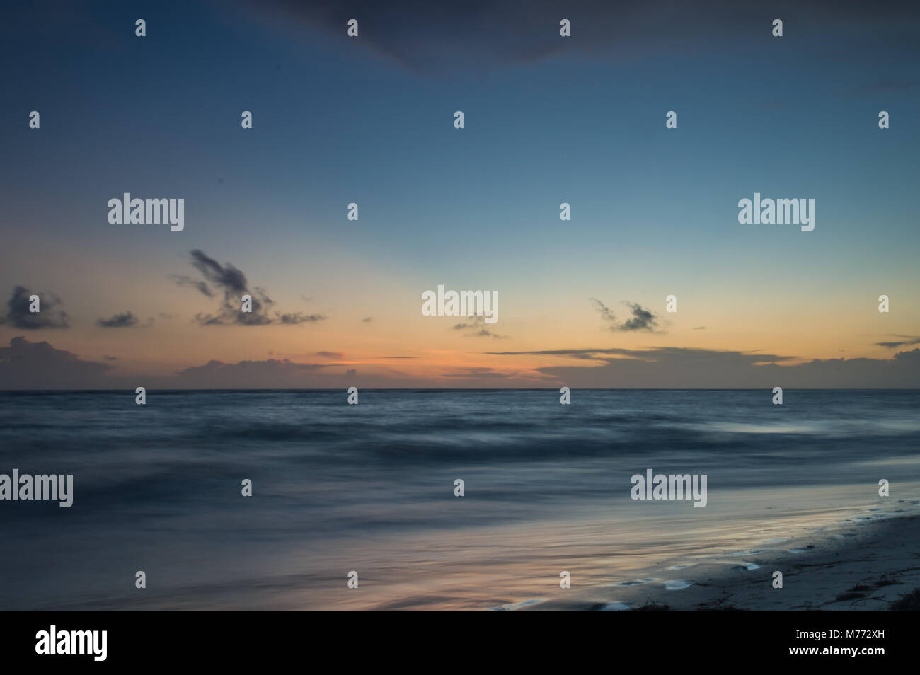 Una lunga esposizione del mare al golden ora come Dawn comincia a rompersi su una spiaggia di sabbia bianca. Foto Stock