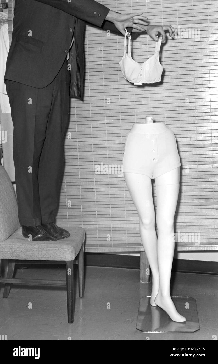 Un 1960s uomo detiene una donna costume da bagno insieme al completamento di una visualizzazione di una donna, ca. 1964. Foto Stock