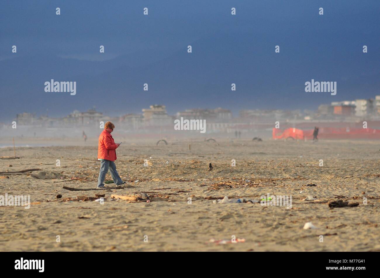 Donna matura usando il telefono in una spiaggia inquinati Foto Stock