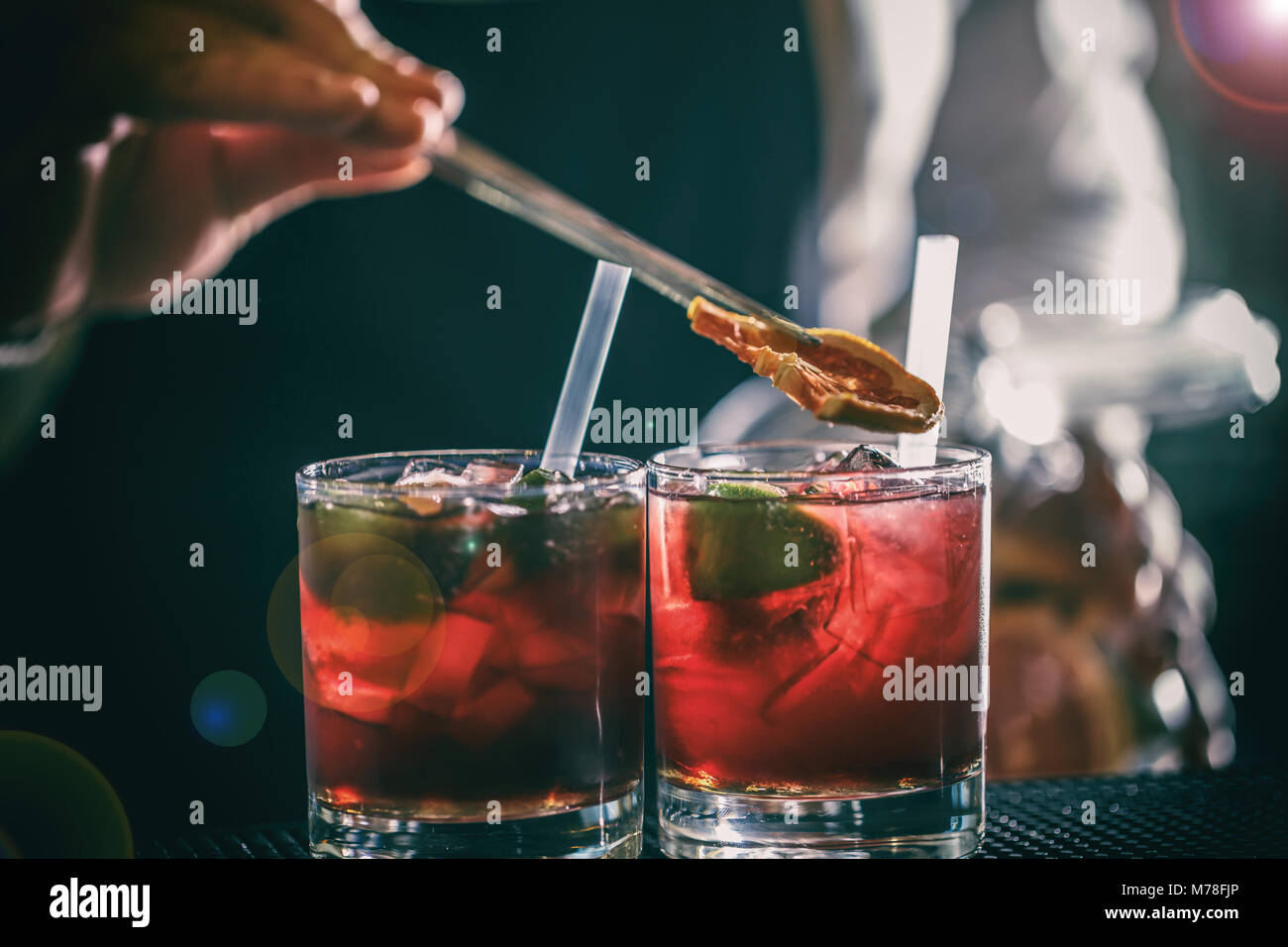 Il barista è aggiunta di limone al red cocktail al bancone bar Foto Stock