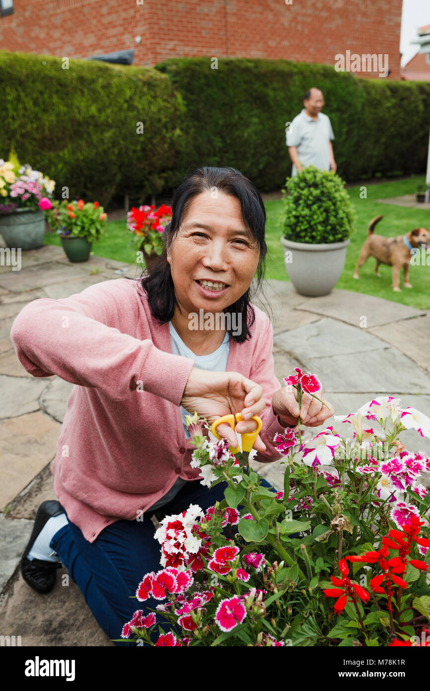Senior donna è sorridere per la fotocamera mentre la potatura di fiori nel suo giardino. Foto Stock