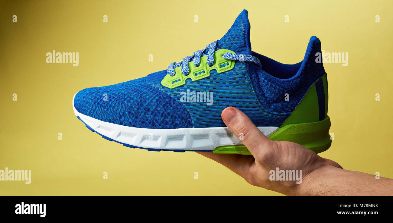 Scarpa sportiva giaceva sul lato isolato su sfondo giallo. Primo piano della coloratissima esercizio scarpa in mano Foto Stock