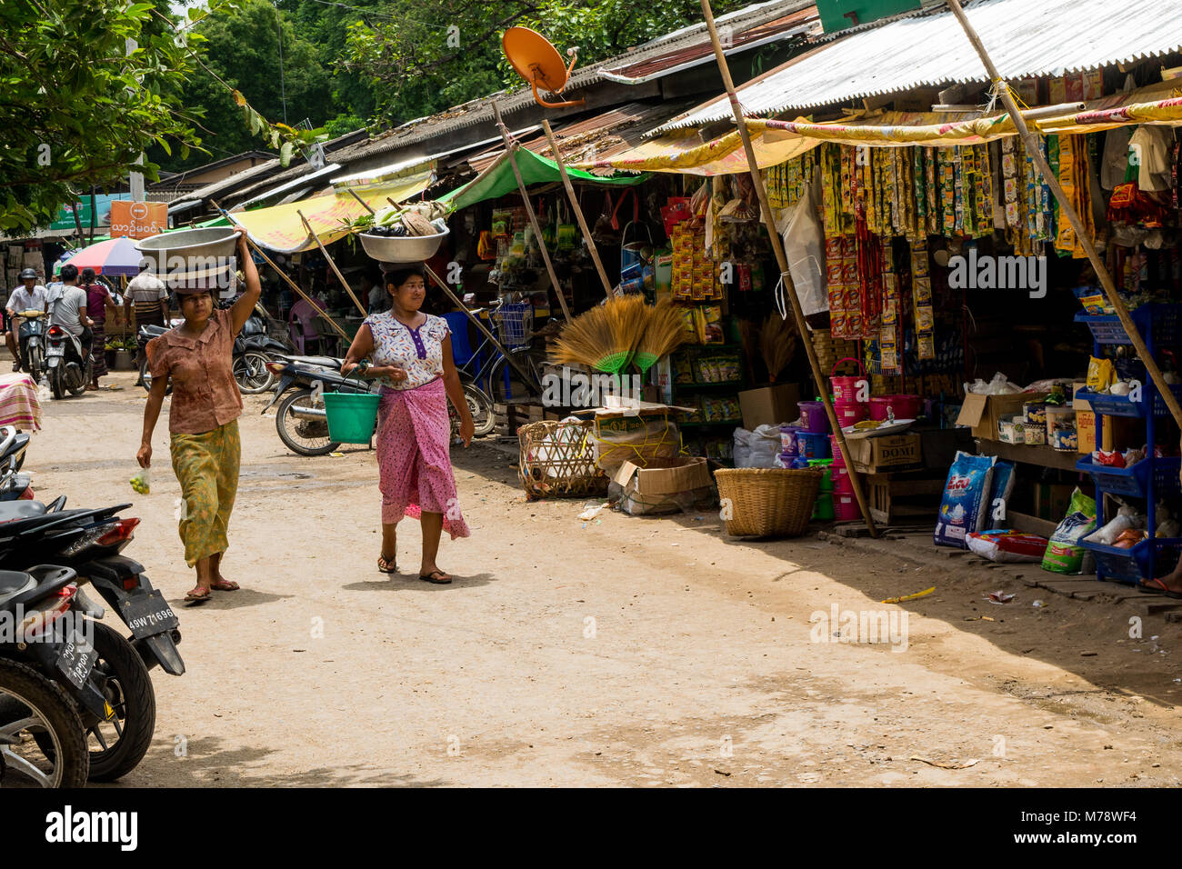 Due donne birmane, lo shopping di Nyaung U mercato locale, testa per trasportare il bilanciamento di un bacino con negozi di generi alimentari sulla loro testa vicino a Bagan, Myanmar, antica Birmania Asia Foto Stock
