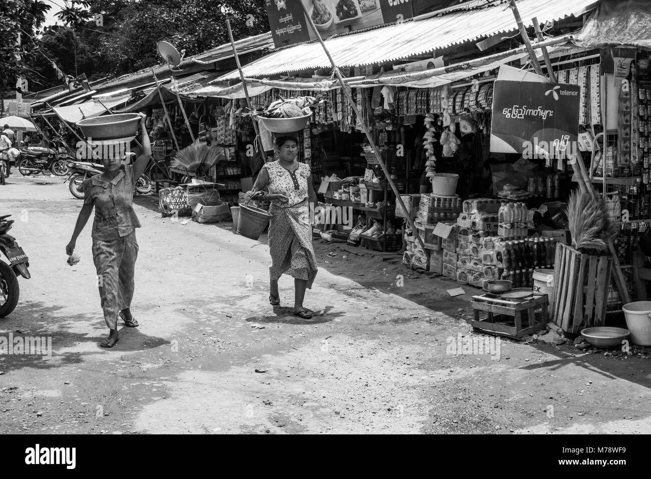 Due donne birmane, lo shopping di Nyaung U mercato locale, testa per trasportare il bilanciamento di un bacino con negozi di generi alimentari sulla loro testa vicino a Bagan, Myanmar, antica Birmania Asia Foto Stock
