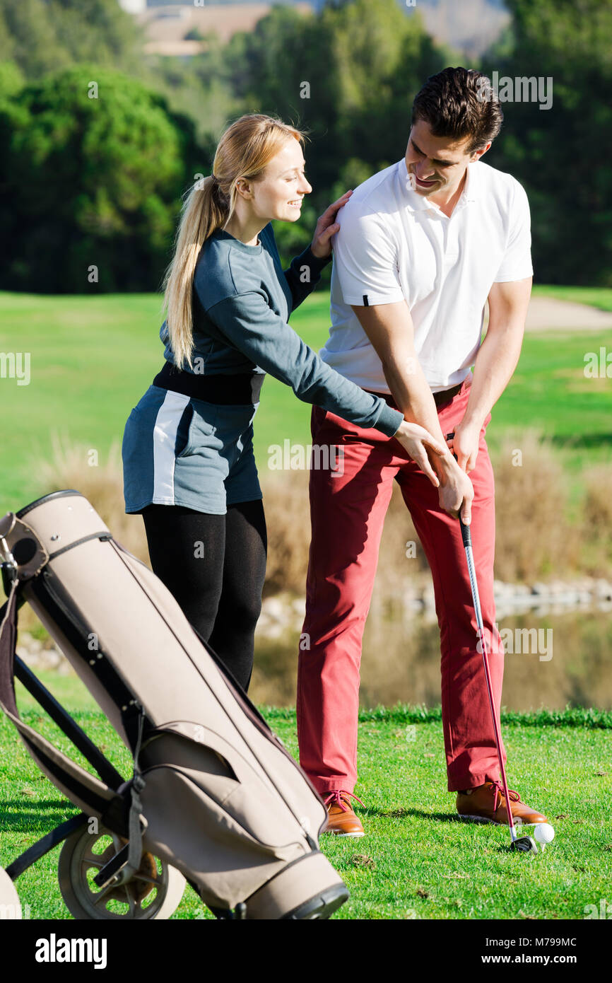 Positivo donna giovane golfista uomo di formazione per giocare a golf e colpire la sfera correttamente Foto Stock