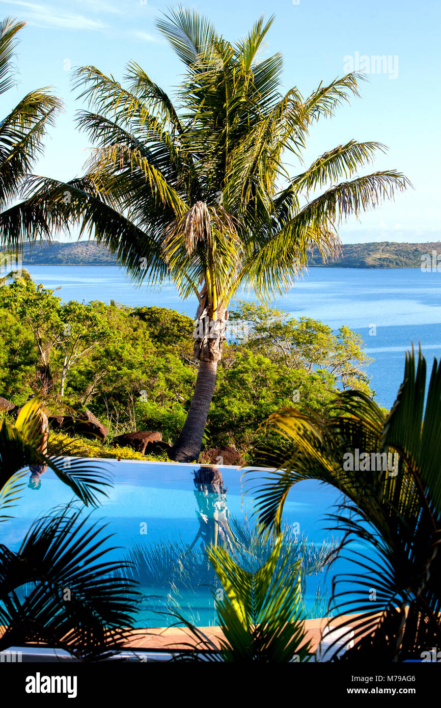 Oceano e colline sullo sfondo si affacciano sulla piscina e palme da cocco sulla struttura isola Fiji durante il giorno caldo e soleggiato. Foto Stock