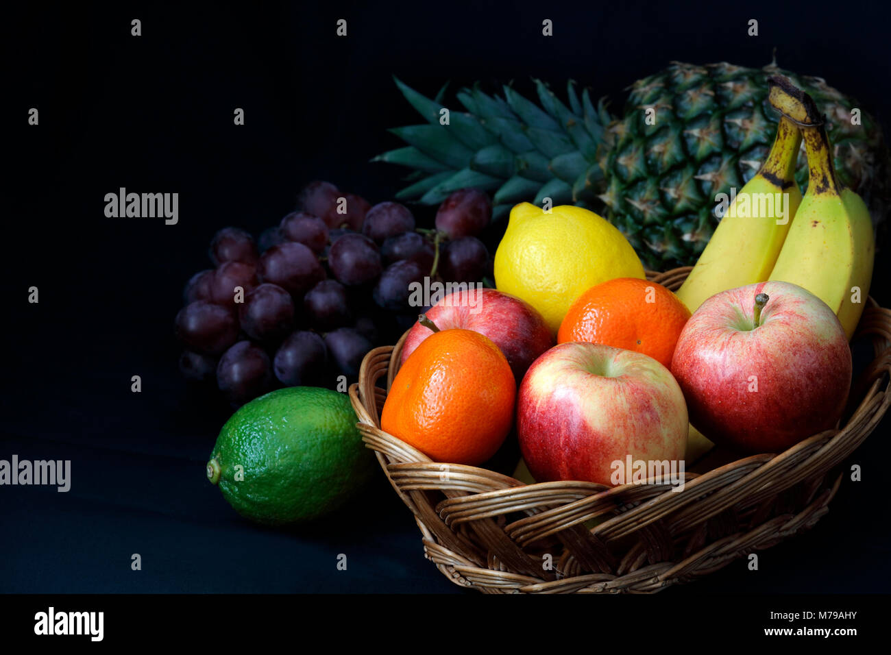 Cibo scuro - Chiaroscuro frutta mista nel cesto di vimini con sfondo scuro con copia spazio a sinistra Foto Stock