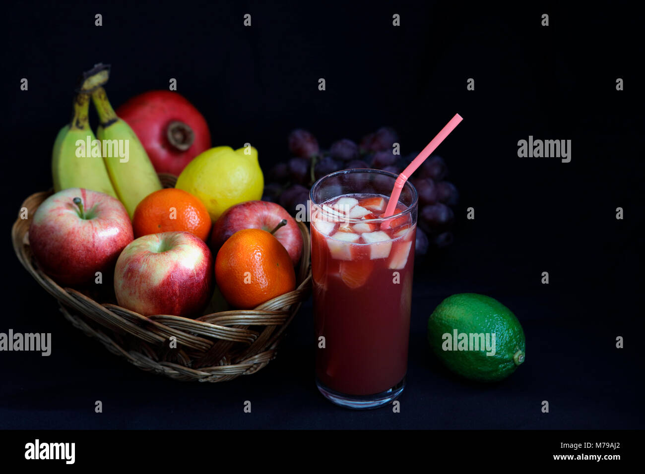Cibo scuro - Chiaroscuro frutta mista nel cesto di vimini con punch alla frutta con sfondo scuro e spazio di copia Foto Stock