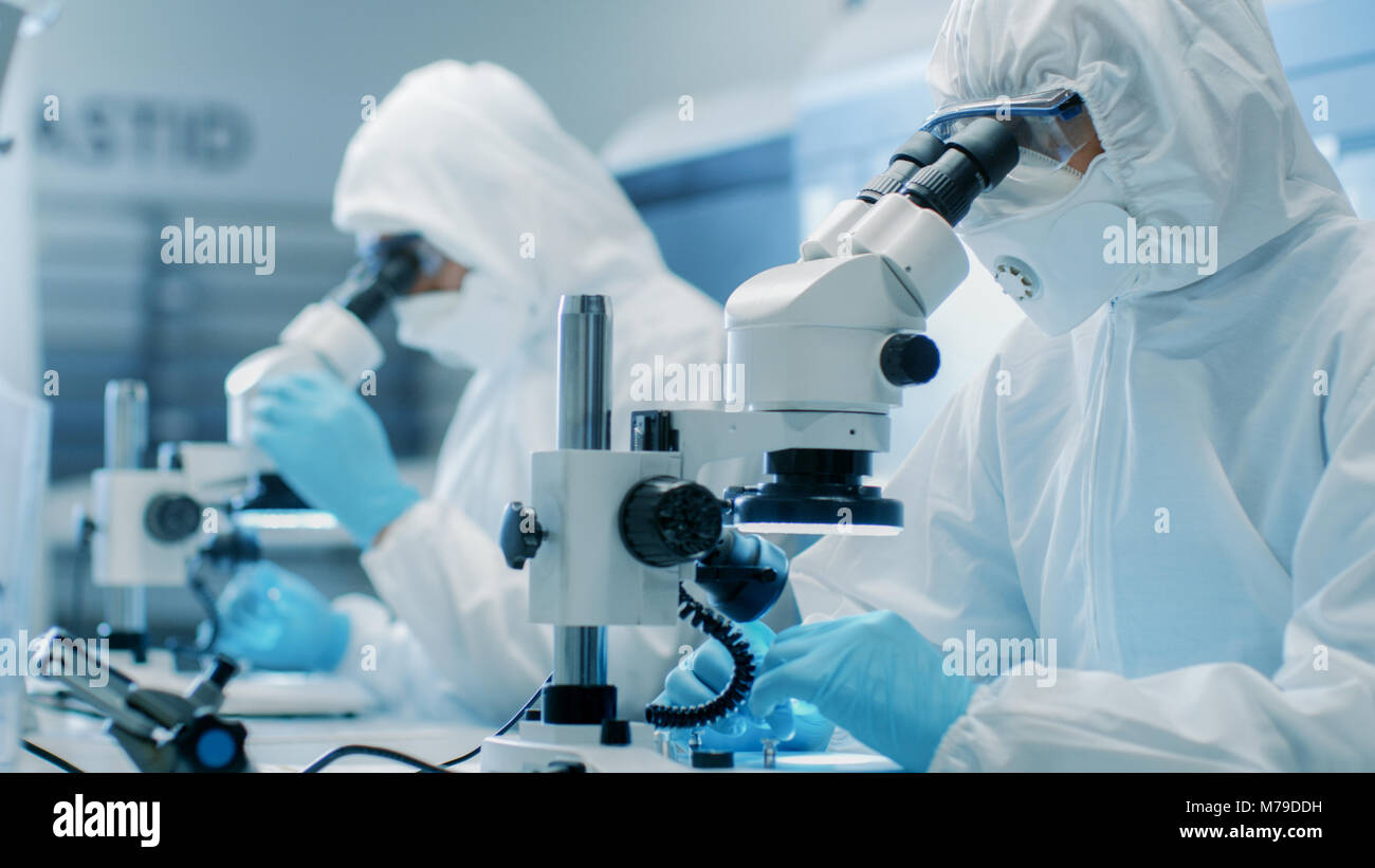 Due ingegneri/ scienziati/ tecnici in sterili per cleanroom utilizzare tute di microscopi per l'organo di regolazione e di ricerca. Essi lavorano in un laboratorio moderno Foto Stock