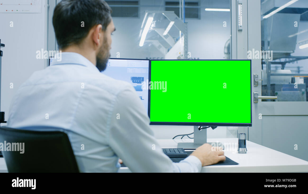 Ingegnere/ tecnico che lavora su un Personal Computer con due schermi, uno ha una schermata verde Chroma Key grande modello per mockup. Foto Stock