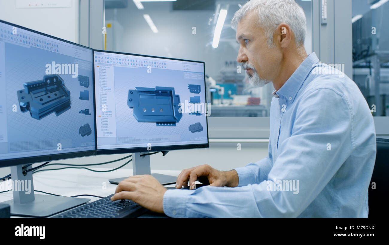 Ingegnere di lavoro su un Personal Computer con due schermi, lui sta progettando un nuovo componente essenziale nel programma CAD. Al di fuori della finestra di ufficio componenti Foto Stock