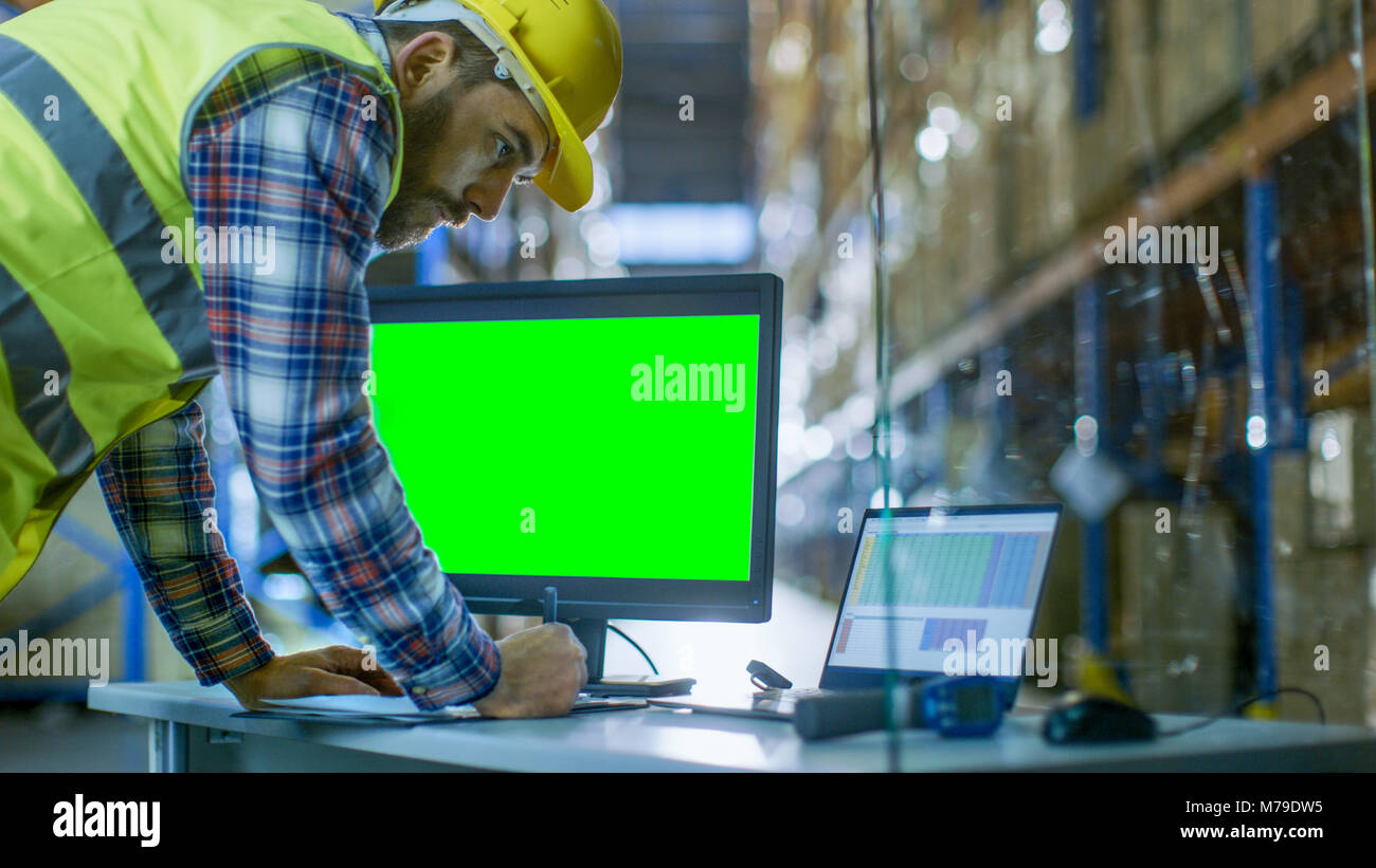 Ispettore maschio riempie i fogli di calcolo sul Suo Personal Computer con schermo verde modello grande per mockup. Egli è nel grande magazzino con righe Foto Stock