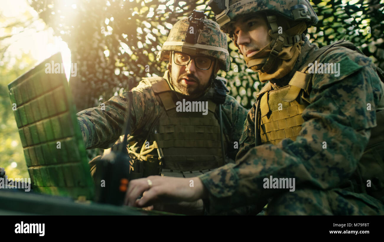 Militare Base di staging, funzionario dà gli ordini al Chief Engineer, essi utilizzare la radio e il grado dell'esercito, portatile. Essi sono in mimetizzata tenda in una foresta. Foto Stock