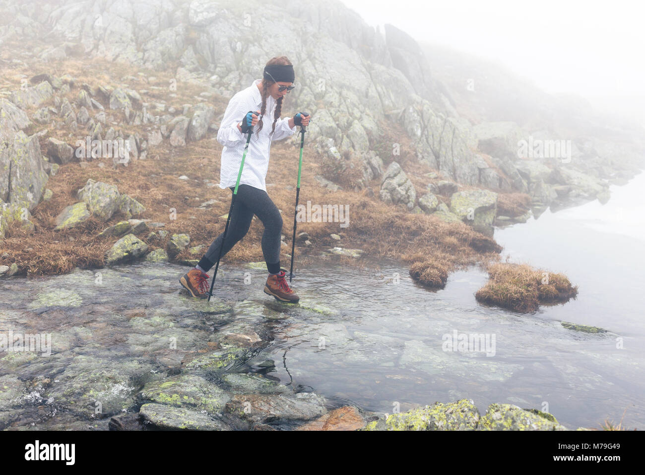 La ragazza si sposta attraverso il fiume in un terreno roccioso nella nebbia meteo. Paesaggio selvaggio di nuvole. Il concetto di stile di vita, avventura, divertimento e Foto Stock