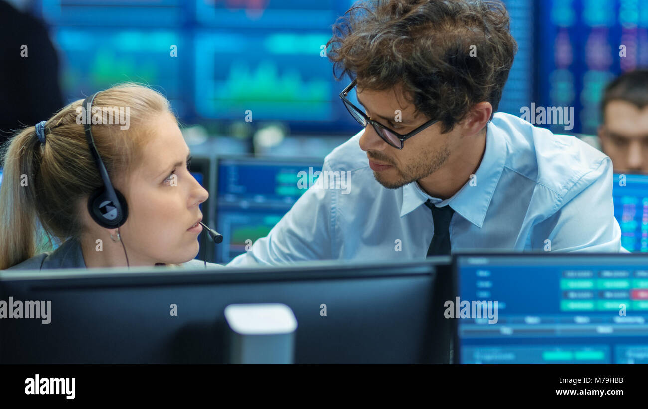 Sperimentato Stock Exchange Trader insegna al suo apprendista presso la sua postazione di lavoro. Team Multi-Ethnic a Stock Exchange Office è occupato. Foto Stock