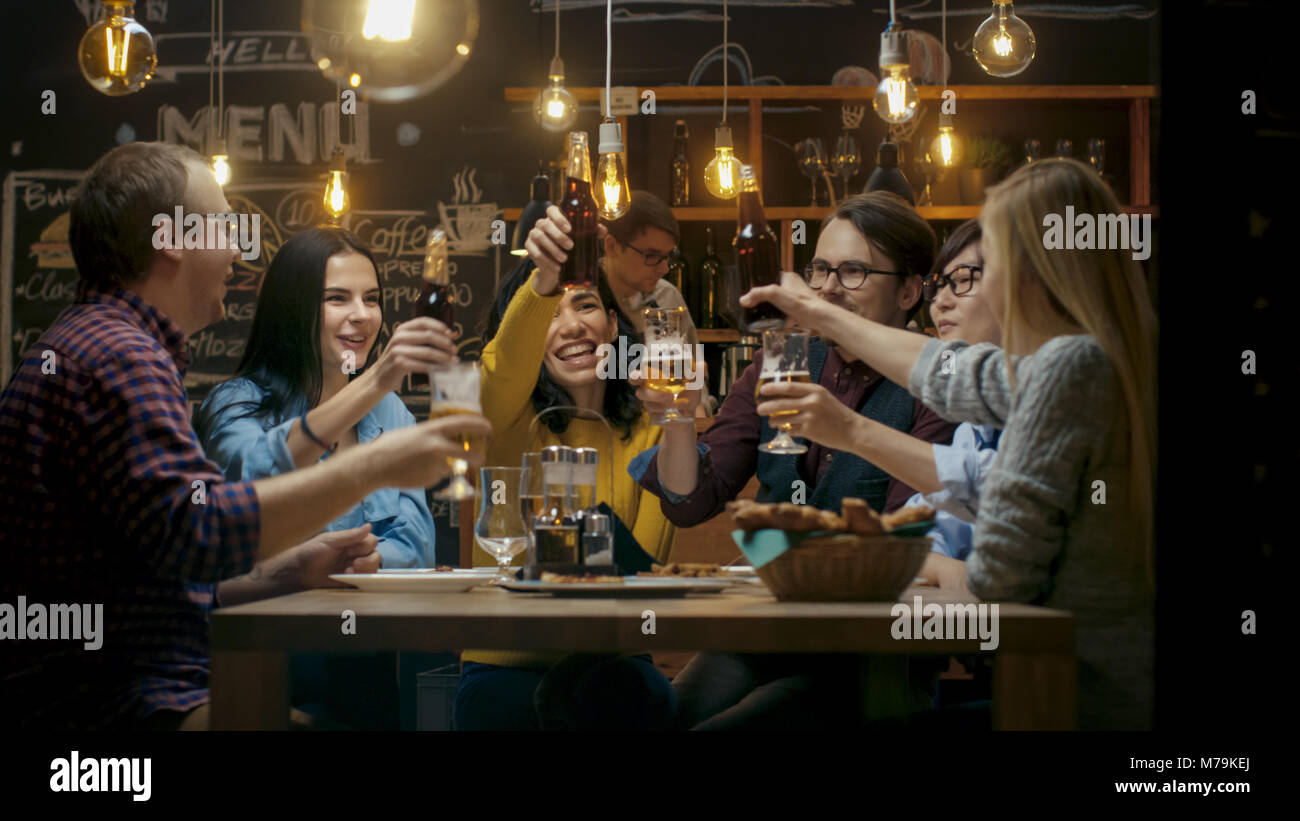 Diversi gruppi di amici festeggiare con un brindisi e il Clink sollevato bicchieri con bevande varie nella celebrazione. Bella Giovani Divertirsi Foto Stock