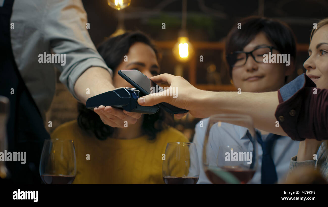 Nel Bar cameriere detiene il pagamento con carta di credito e della macchina e uomo paga per il suo ordine con Contactless Telefono Mobile sistema di pagamenti. Egli ha buon tempo Foto Stock