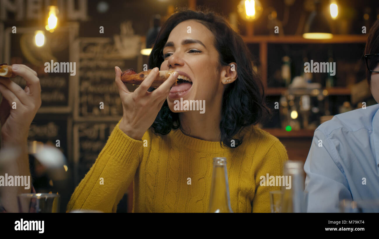 Bella Donna ispanica mangia trancio di pizza presso il ristorante elegante. Lei è circondato dai suoi amici. Foto Stock