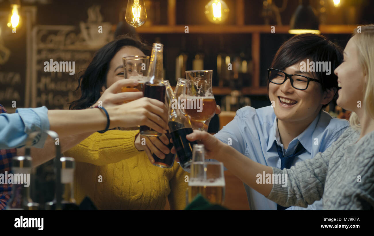 Gruppo diversificato di splendidi giovani fare un brindisi e Clink sollevato bicchieri con bevande varie nella celebrazione. Foto Stock