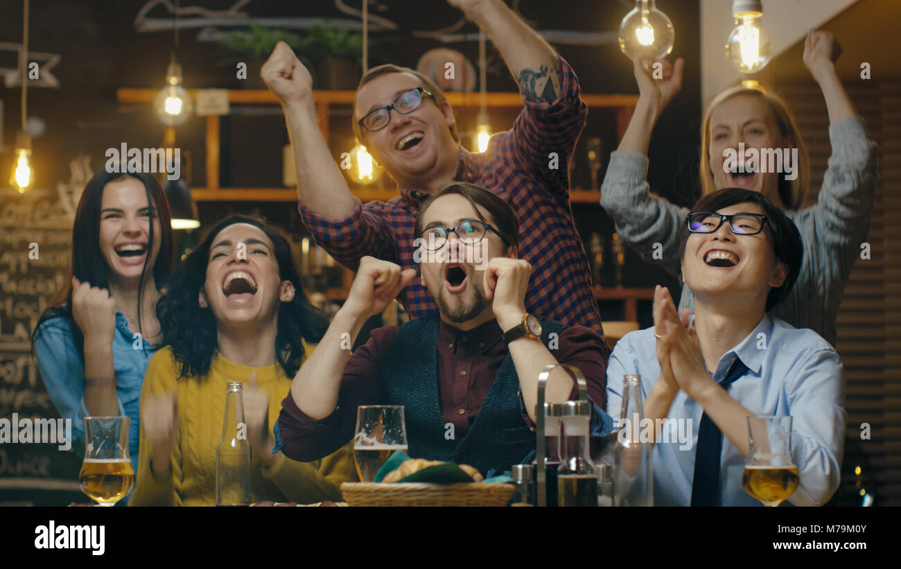 Diversi gruppi di amici Orologi TV in Sporstbar. Bella Giovani bere, avere divertimento e allegria per i loro team. Foto Stock