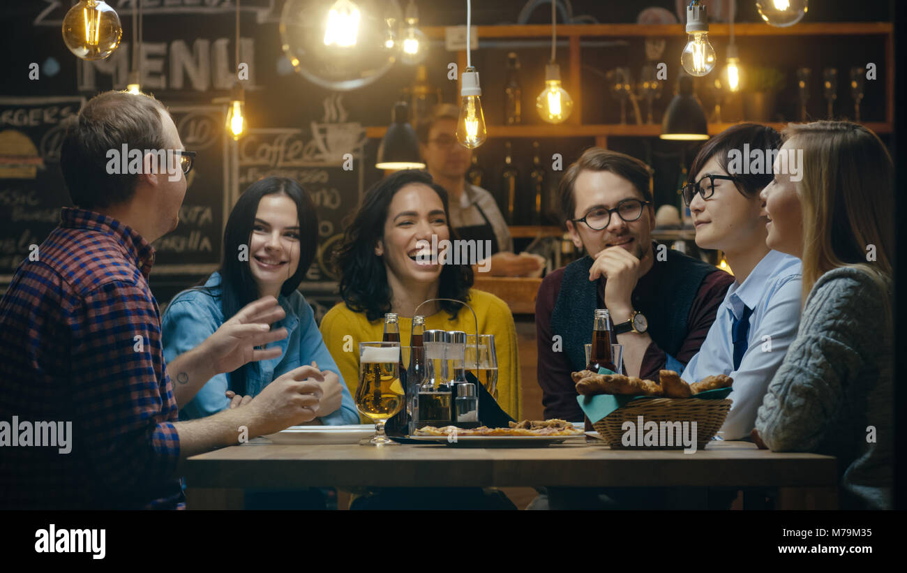 Diversi gruppi di giovani hanno divertimento nel bar, parlando, raccontare storie e barzellette. Non bere bevande varie. Si trovano in un elegante Hipster Bar Foto Stock