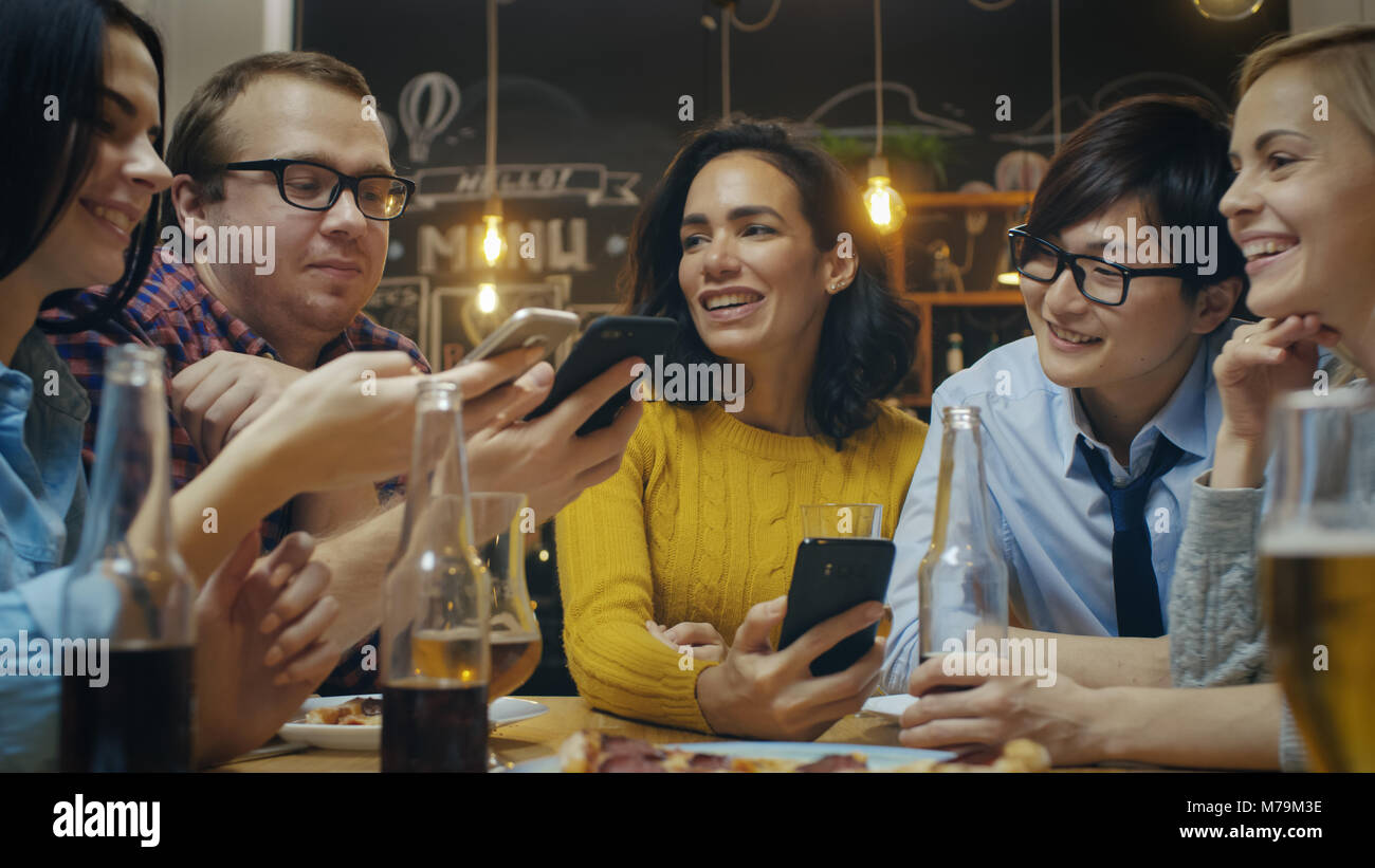 Nel Bar/Ristorante variegato gruppo di amici hanno una buona volta la condivisione di foto e whatnot con il loro smartphone. Bella gente nel bar elegante Foto Stock