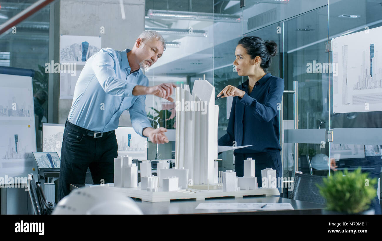 Due professionale maschio e femmina ingegneri architettonico lavorare con Blueprint e su un modello di edificio di design per la pianificazione urbana progetto. Foto Stock