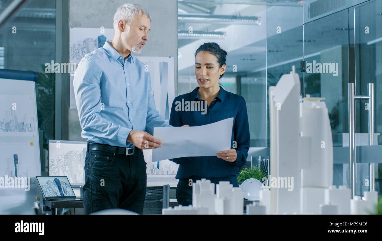 Due professionale maschio e femmina ingegneri architettonico lavorare con blueprint, discutendo la costruzione di modello di progettazione per la pianificazione urbana progetto. Foto Stock