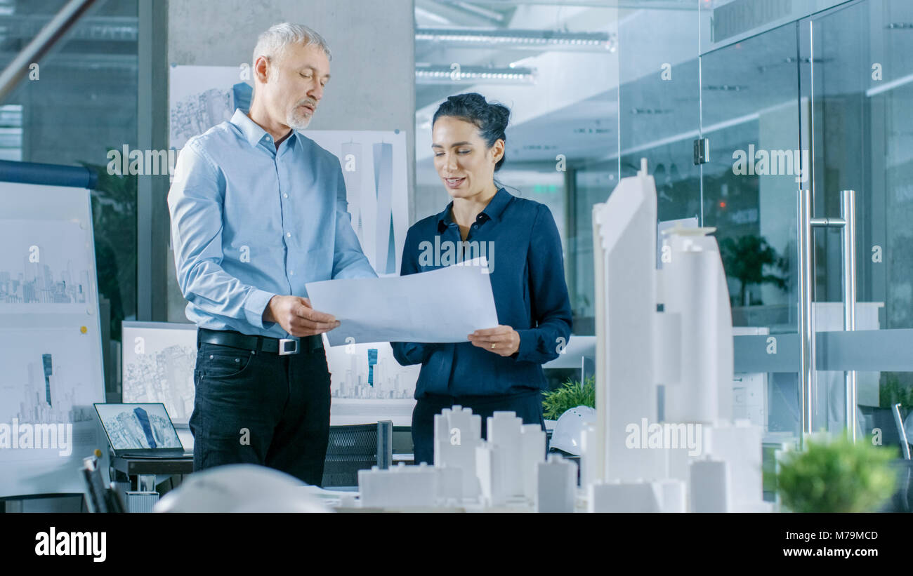 Due professionale maschio e femmina ingegneri architettonico lavorare con blueprint, discutendo la costruzione di modello di progettazione per la pianificazione urbana progetto. Foto Stock