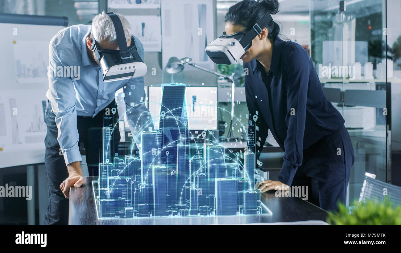 Maschio e femmina di architetti che indossa la realtà aumentata auricolari funzionano con il modello 3D della città. High Tech Office Professional persone utilizzano la realtà virtuale modello Foto Stock