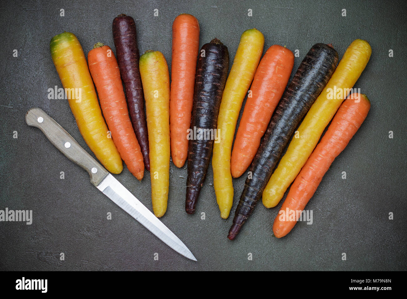 Verdure colorate. Organici di colore giallo, rosso, arancione e viola le carote in pietra scura superficie. Stile rustico Foto Stock