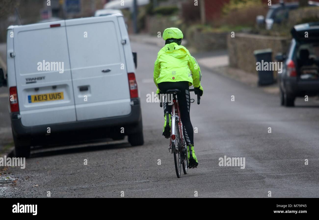 Un ciclista in un hi-vis giacca passeggiate intorno a un furgone su una strada. Foto Stock