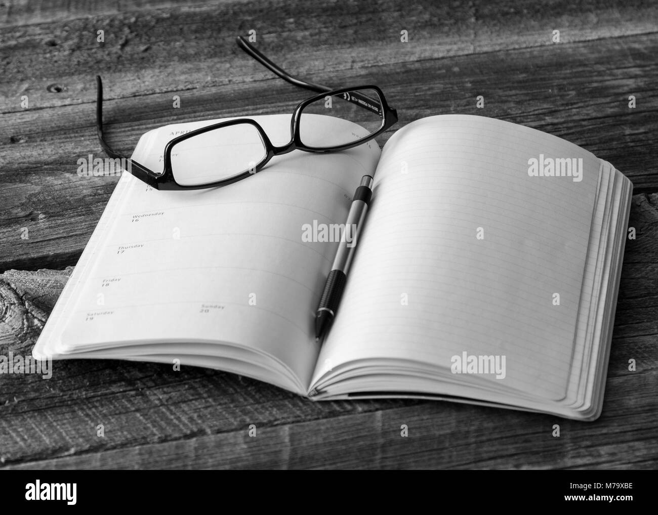 Planner e matita con una coppia di nero occhiali bordati su una tavola in legno rustico, concetto di business Foto Stock