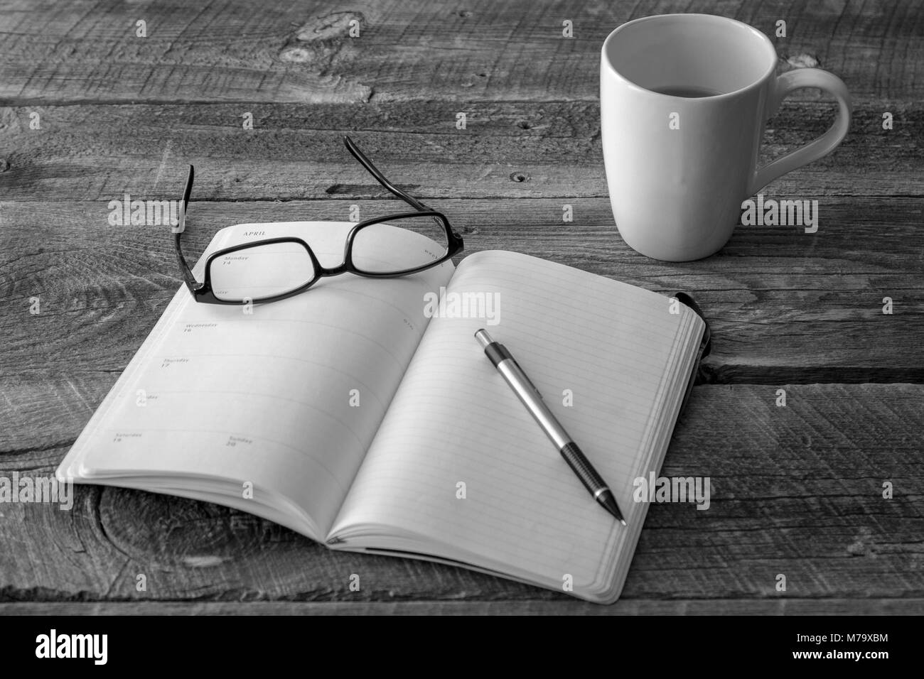 Planner e matita con una coppia di nero bordati di occhiali e la tazza di caffè su una tavola in legno rustico, concetto di business Foto Stock