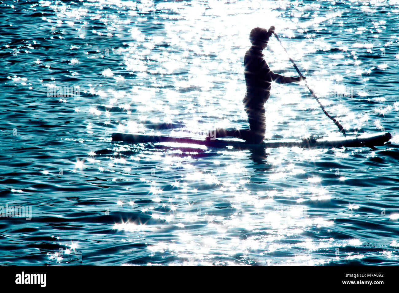 Sfocata silhouette di un uomo inginocchiato sulla scheda di racchetta e canottaggio al chiaro di luna illuminata mare, facendo sport di acqua ricreazione per il corpo e per la mente Foto Stock