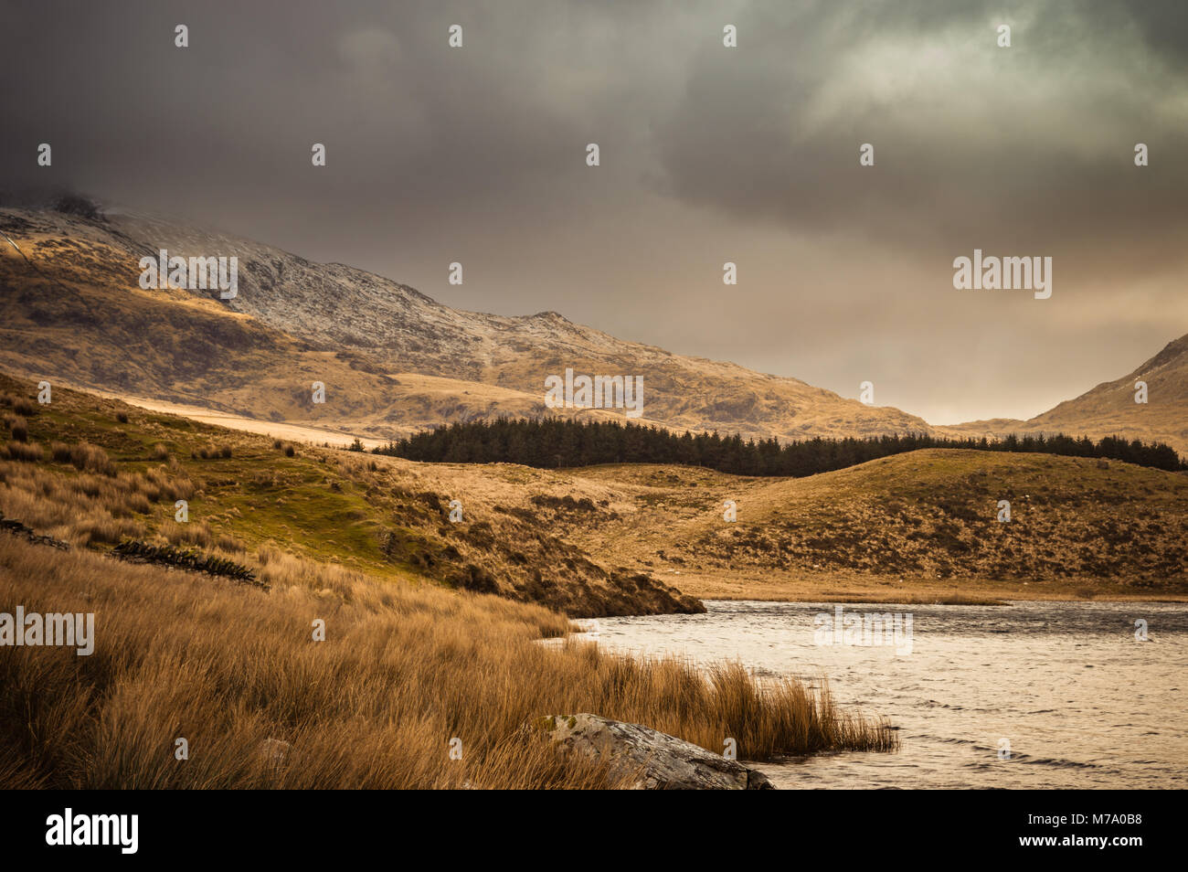 Vista sul lago al Snowdon Horseshoe a Llyn Y Dywarchen, come il sole illumina il fianco della montagna nel Parco Nazionale di Snowdonia, Galles. Foto Stock