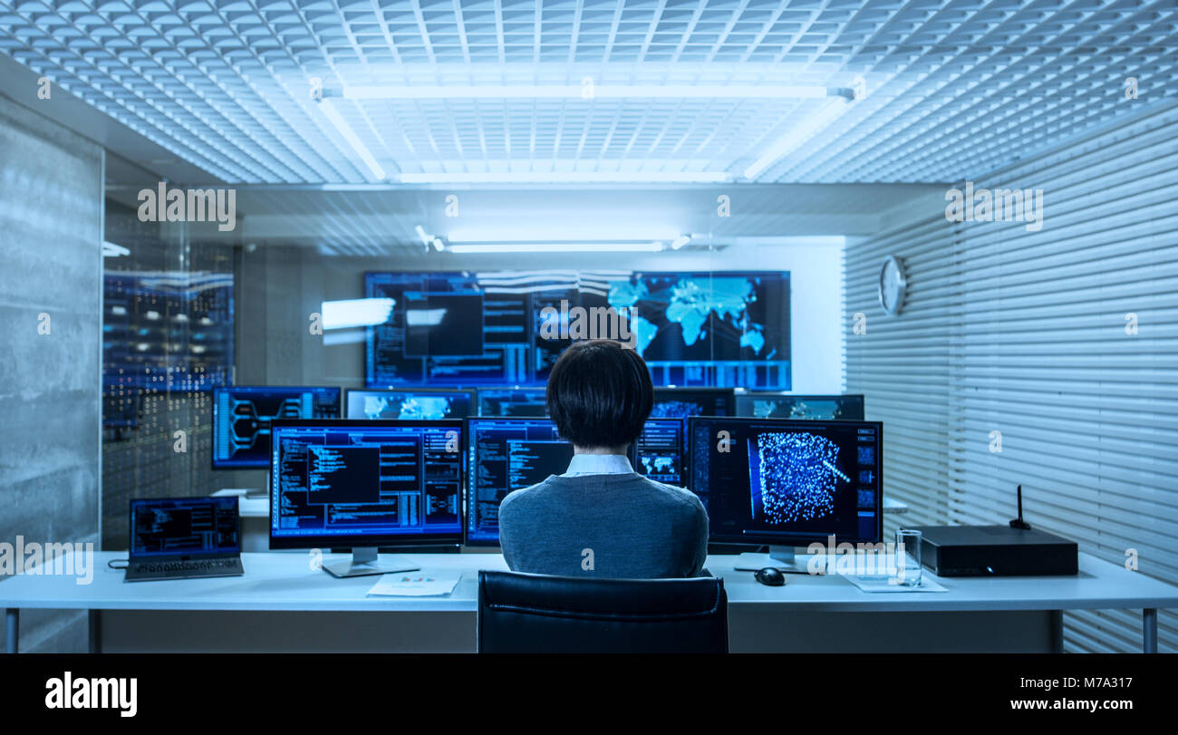 Vista posteriore dell'Ingegnere IT lavora con più monitor che mostra la grafica e funzionale della rete neurale. Egli lavora in un tecnologicamente avanzato Foto Stock