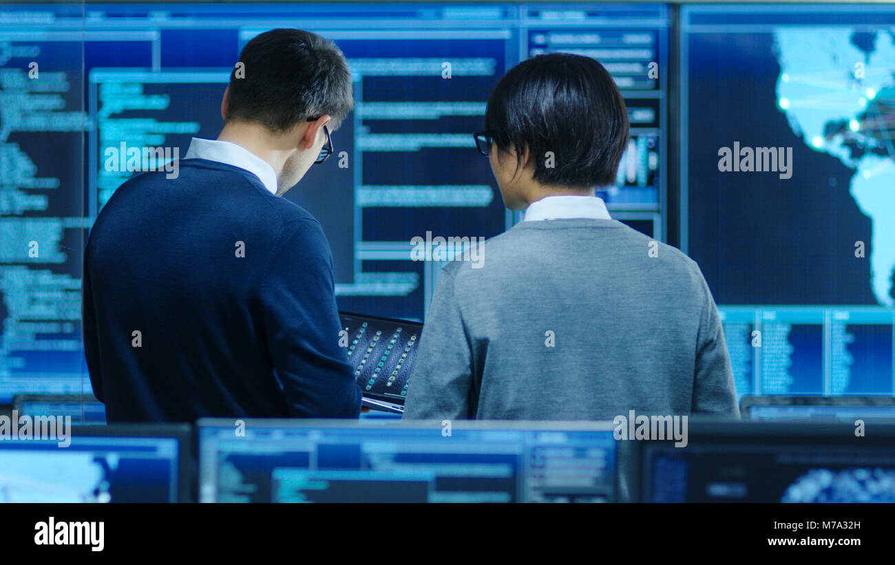 Nel sistema della sala di controllo dello specialista IT e Project Engineer hanno discussione, sono circondati da più monitor con grafica. Foto Stock