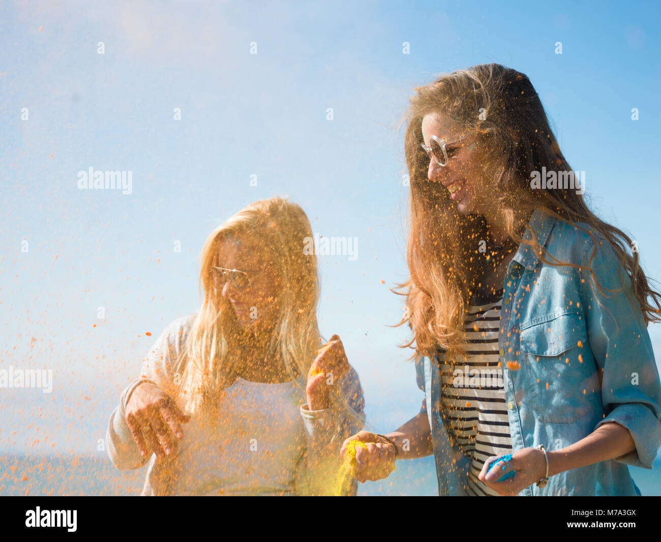 Due belle ragazze felici celebrare Holi festival lanciando polvere colorata in aria e ridere. Sono in riva al mare e hanno un sacco di divertimento. Foto Stock