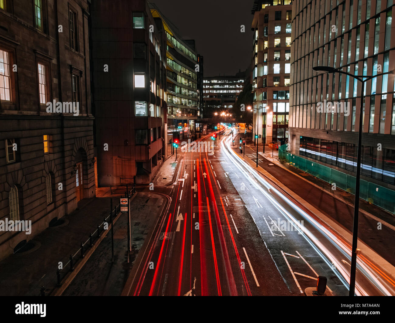 I sentieri di luce sulla costruzione di ufficio background a notte come vetture passando sulla Upper Thames Street a Londra, Regno Unito. Il verde e il rosso semaforo. Foto Stock